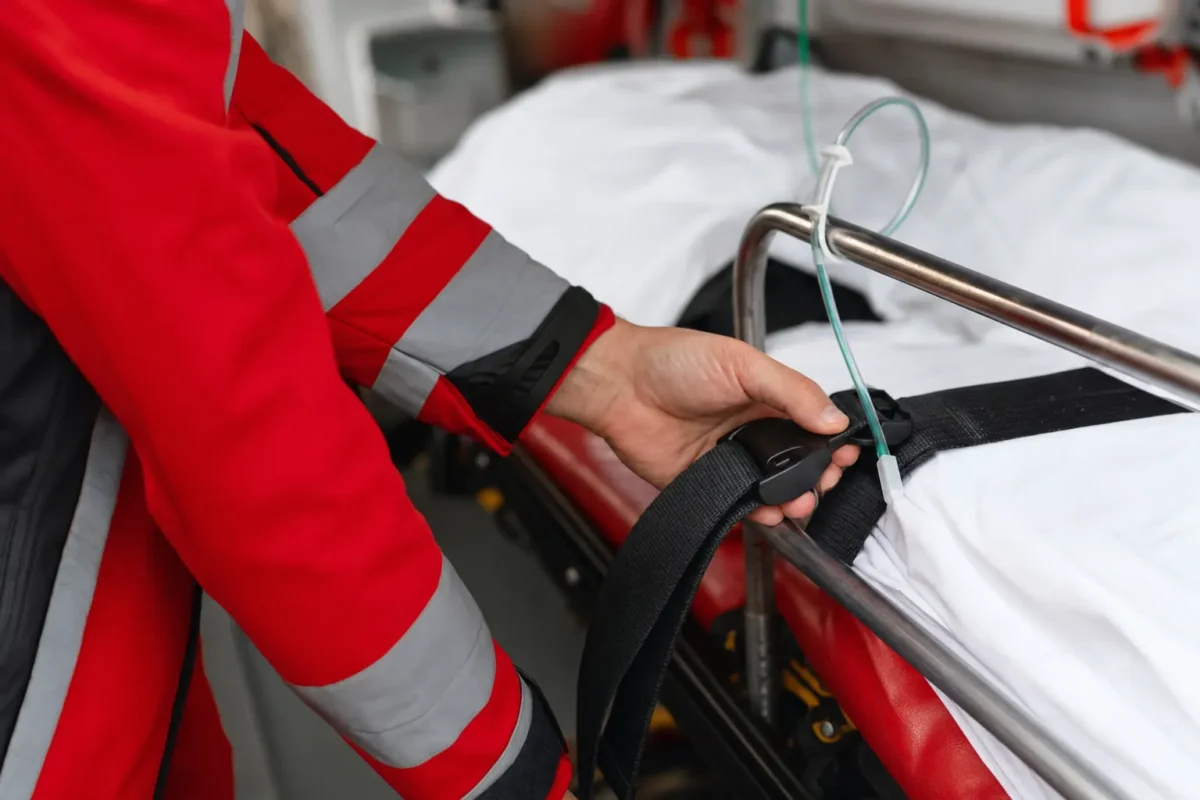 plan serré sur une main refermant une sangle de sécurité sur un brancard, barrière latérale relevée, tubulure d'oxygène