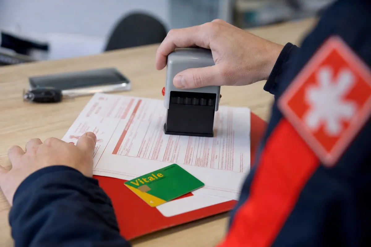 plan serré sur des mains posant un tampon sur un formulaire de bon de transport à côté d'une carte Vitale sur un bureau